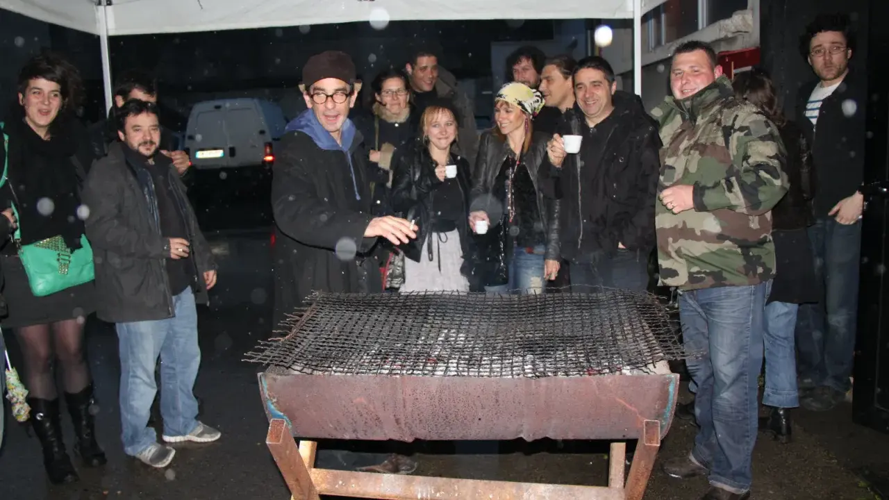Un groupe d'amis profite d'un barbecue sous la pluie, sous un abri. L'ambiance est conviviale malgré les gouttes.