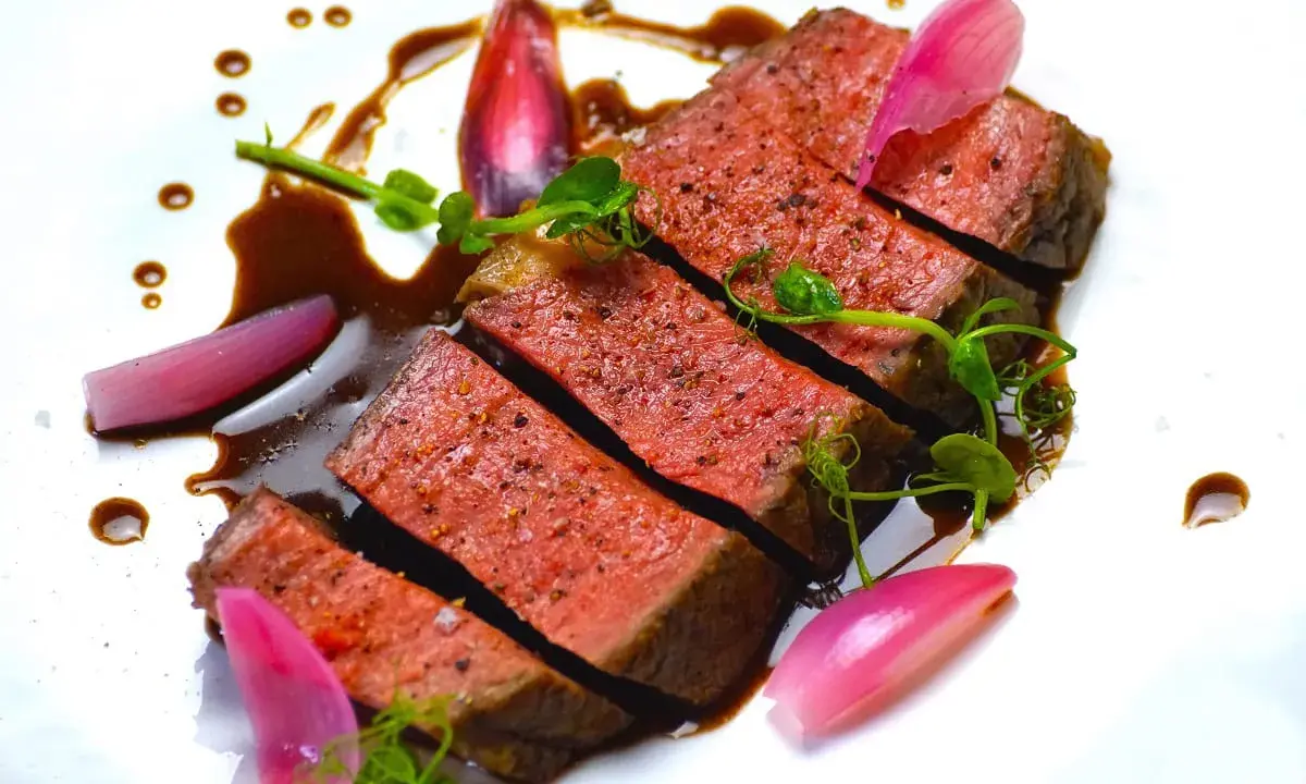 Une succulente entrecôte de bœuf, tranchée et nappée d'une sauce riche, accompagnée de jeunes pousses et d'oignons rouges marinés.