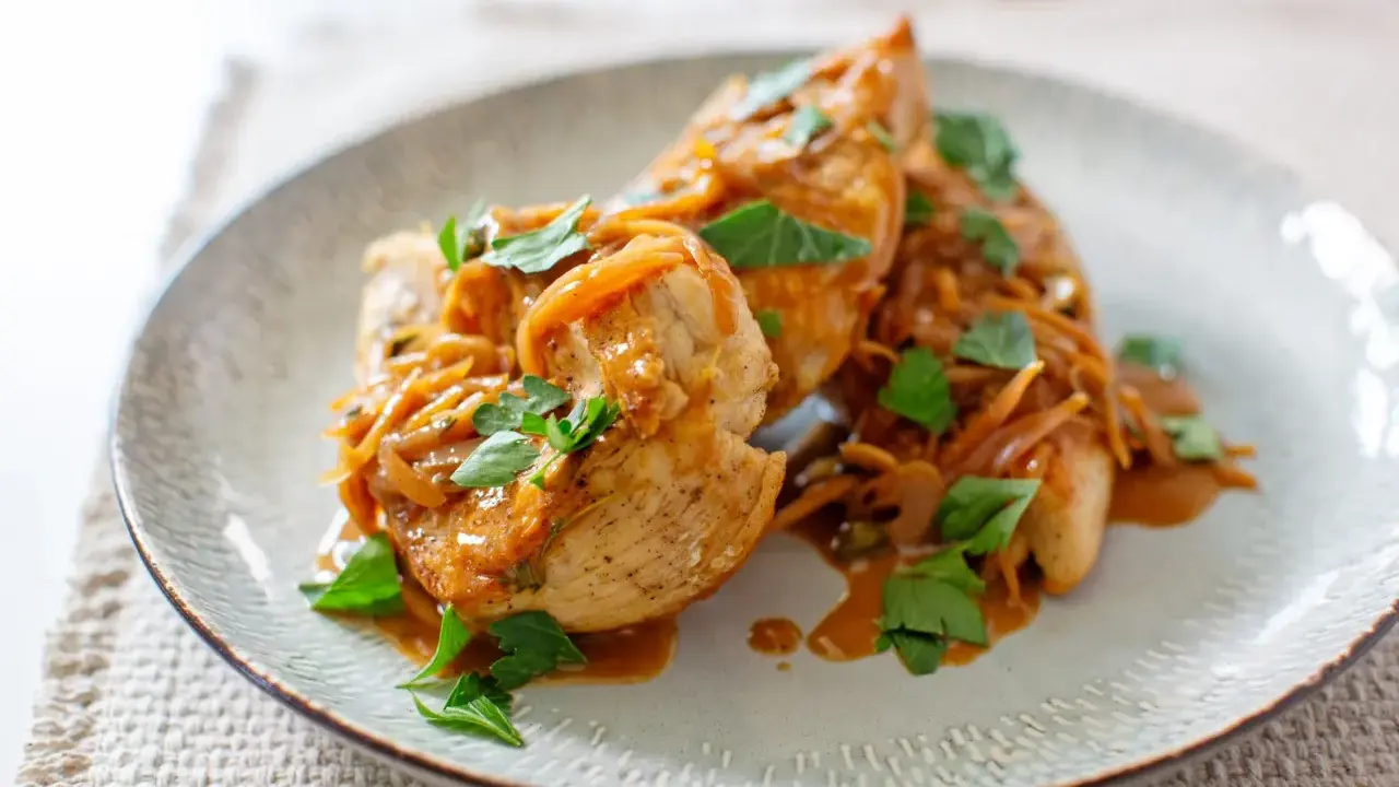 Trois escalopes de poulet nappées d'une sauce onctueuse aux oignons caramélisés et garnies de persil frais. Un plat savoureux et réconfortant.