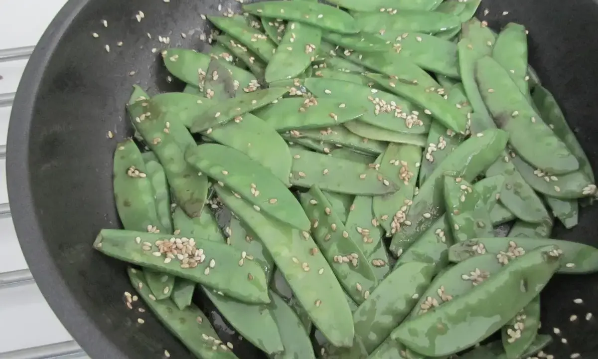 Pois gourmand croquants saupoudrés de graines de sésame dans une poêle.