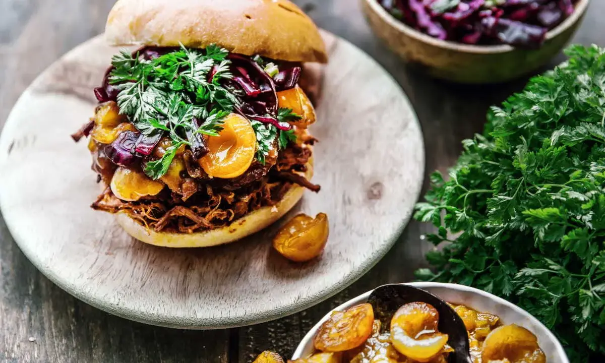 Un délicieux burger de pulled pork garni de fruits et de persil frais, accompagné d'une salade de chou rouge et de fruits confits.