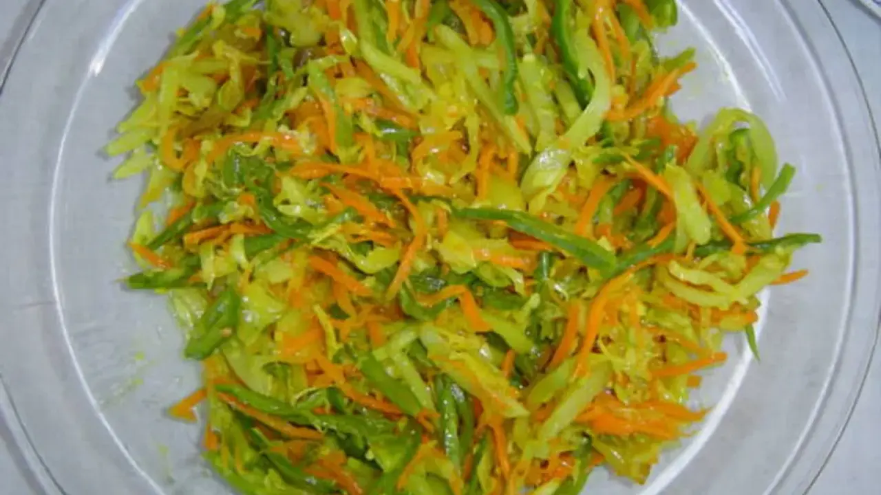Un plat coloré d'achard de légumes, mêlant carottes râpées, chou et poivrons verts, prêt à être dégusté.