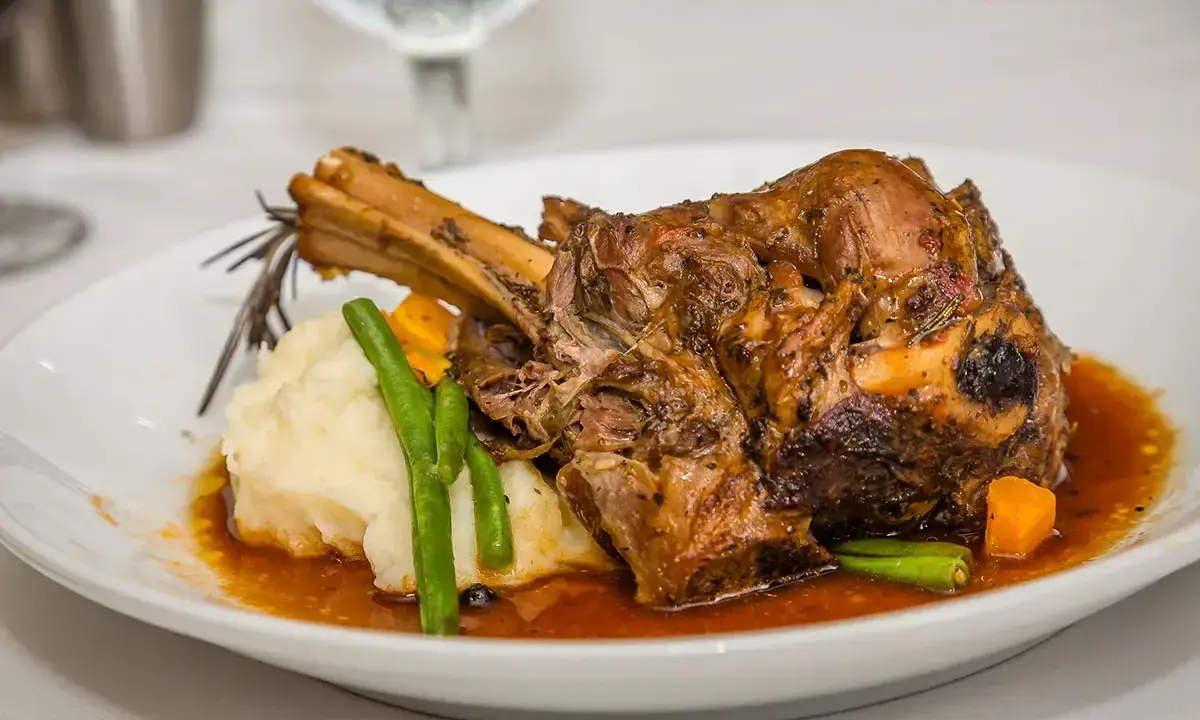 Une souris d'agneau braisée, servie avec une purée onctueuse, des haricots verts croquants et des dés de carottes, le tout nappé d'une sauce savoureuse.