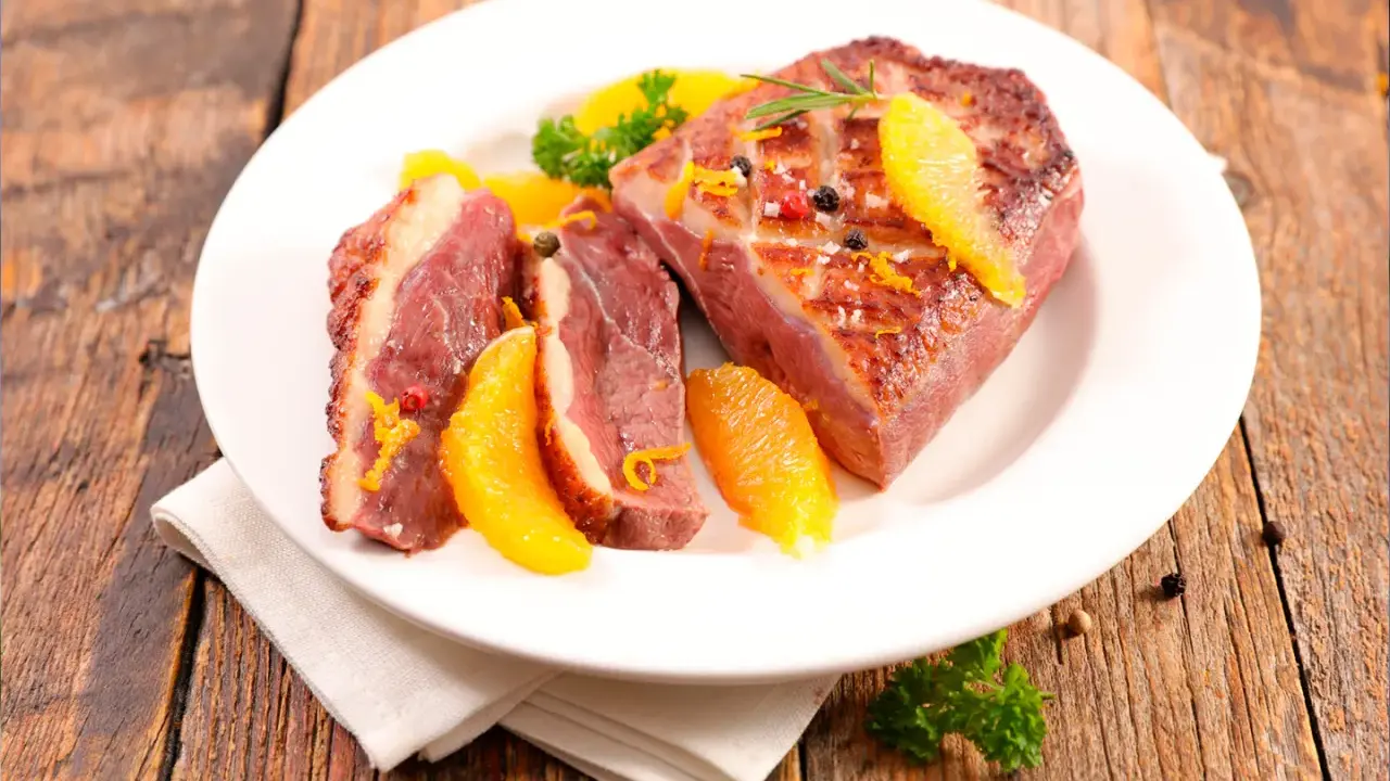 Magret de canard tranché, garni d'orange et de romarin, prêt à être dégusté. Une excellente recette plancha pour un repas savoureux.