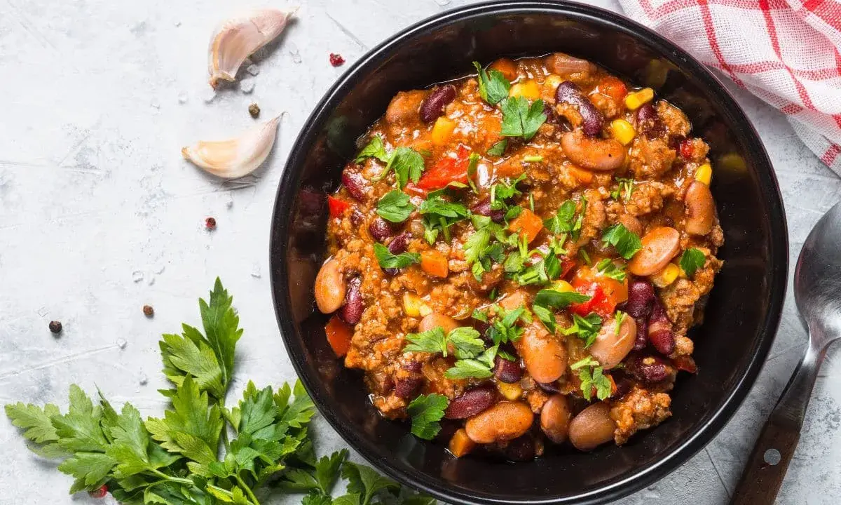 Un bol de chili sin carne, garni de persil frais, avec des haricots rouges, du maïs et des poivrons. Parfait pour un repas réconfortant.