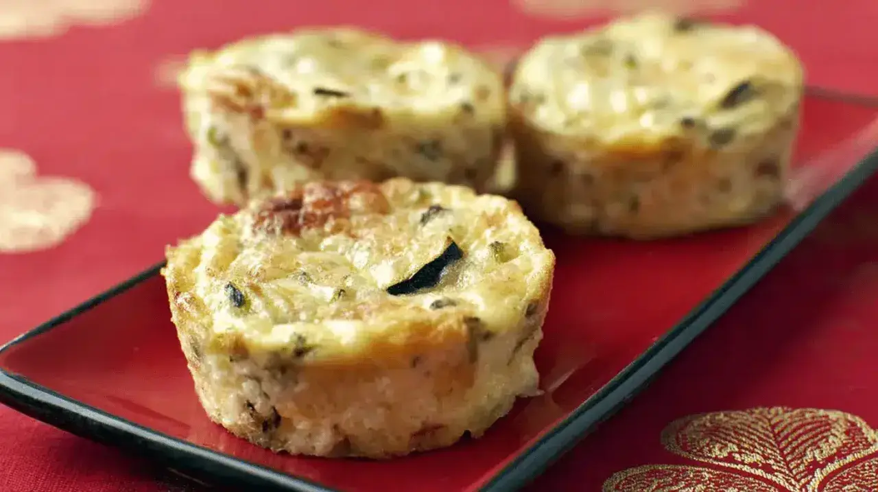 Trois petits flans de courgettes dorés et appétissants sur une assiette rouge, parfaits pour un repas léger.