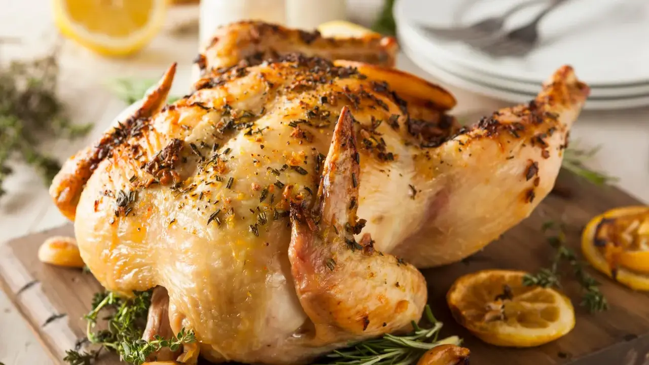 Un délicieux poulet rôti, doré et parfumé aux herbes, est servi sur une planche en bois avec des quartiers de citron et de l'ail rôti.
