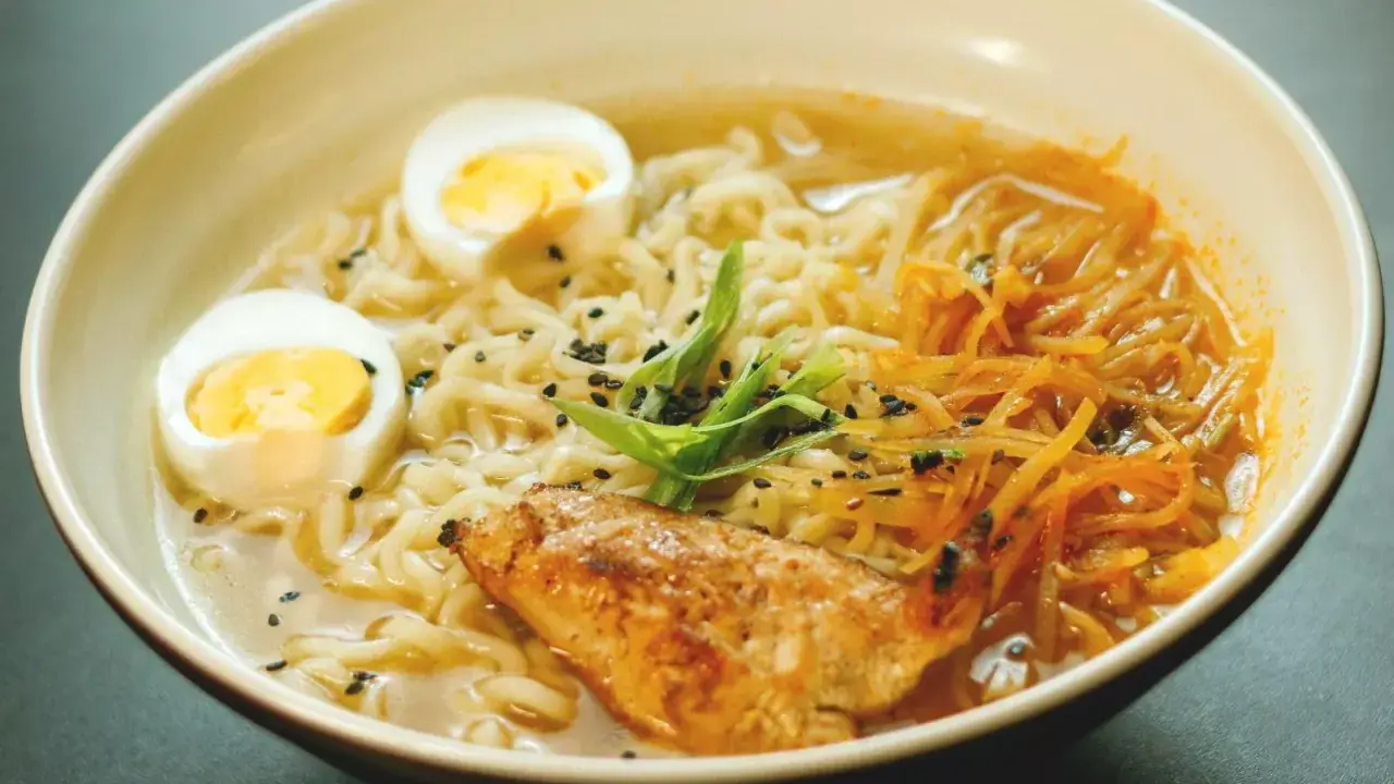Un bol de ramen poulet avec nouilles, œuf dur, poulet grillé, julienne de carottes et oignons verts. Une recette réconfortante.