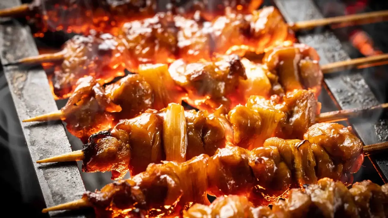 Brochettes de bœuf et fromage grillées sur des braises ardentes, dégageant une fumée alléchante.