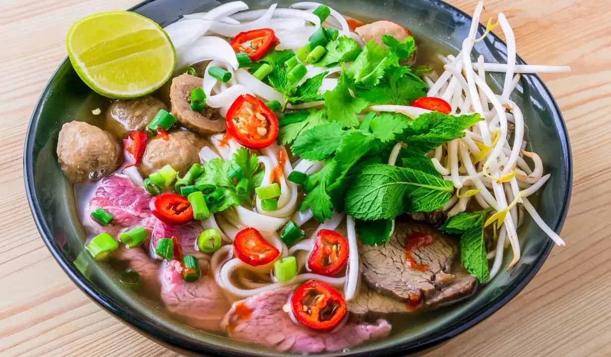 Un bol de soupe pho savoureux avec du bœuf, des boulettes, des nouilles, des herbes fraîches, des piments et un quartier de citron vert.