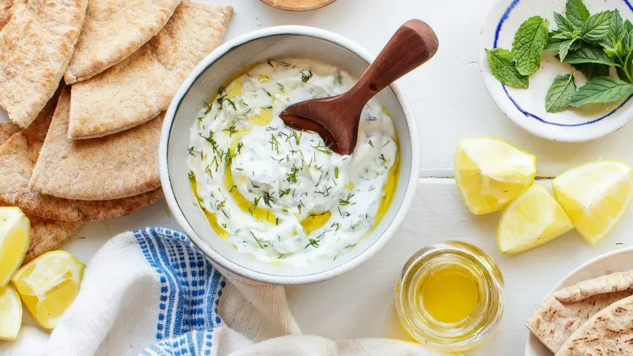 Un bol de tzatziki crémeux, garni d'aneth et d'huile d'olive, prêt à être dégusté avec du pain pita. Une recette fraîche et savoureuse.