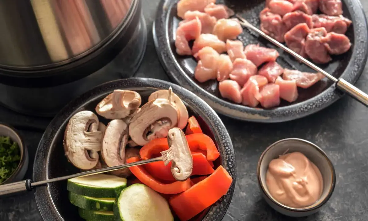 Préparation d'une fondue bourguignonne 3 viandes : cubes de poulet et bœuf crus, champignons, courgettes, poivrons et sauce.