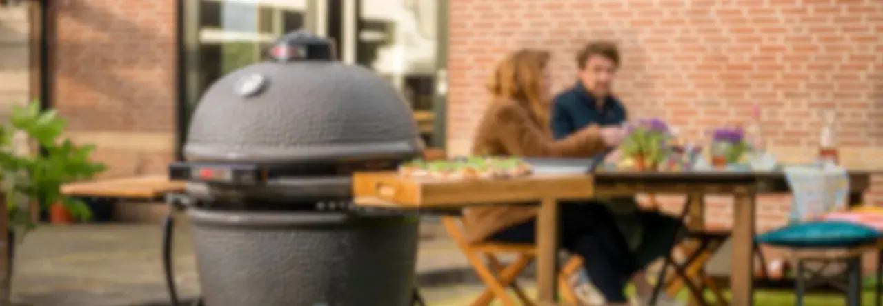 Un couple profite d'un repas en plein air avec une pizza fraîchement préparée, la cuisson kamado promettant une saveur incomparable.