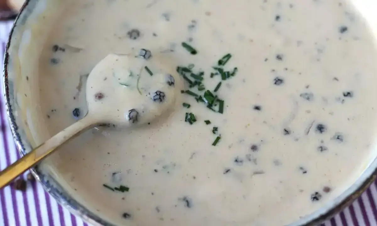 Une cuillère dorée plonge dans une onctueuse sauce au poivre, garnie de ciboulette fraîche.