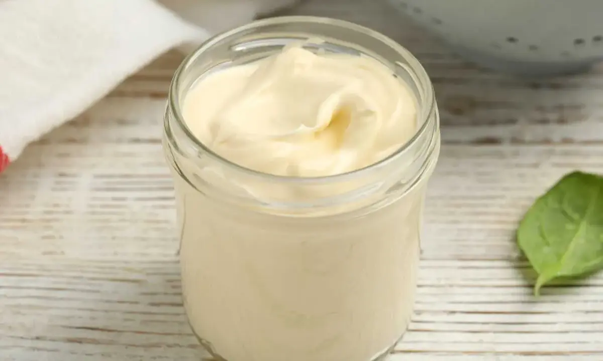 Un pot de mayonnaise sans huile, crémeuse et onctueuse, sur une table en bois. Une feuille verte à côté.
