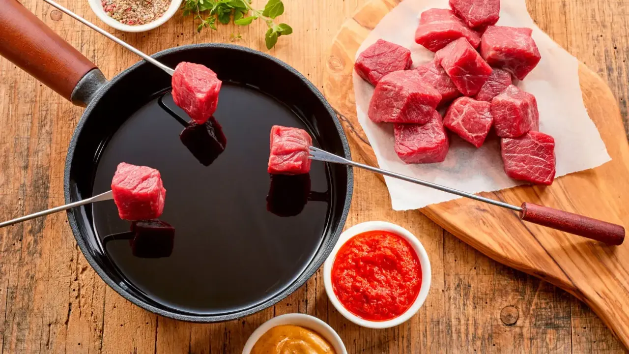 Préparation d'une fondue chinoise : des cubes de viande rouge sur des brochettes trempent dans un bain d'huile chaude. Quel accompagnement fondue viande ? Sauces et épices sont à portée de main.