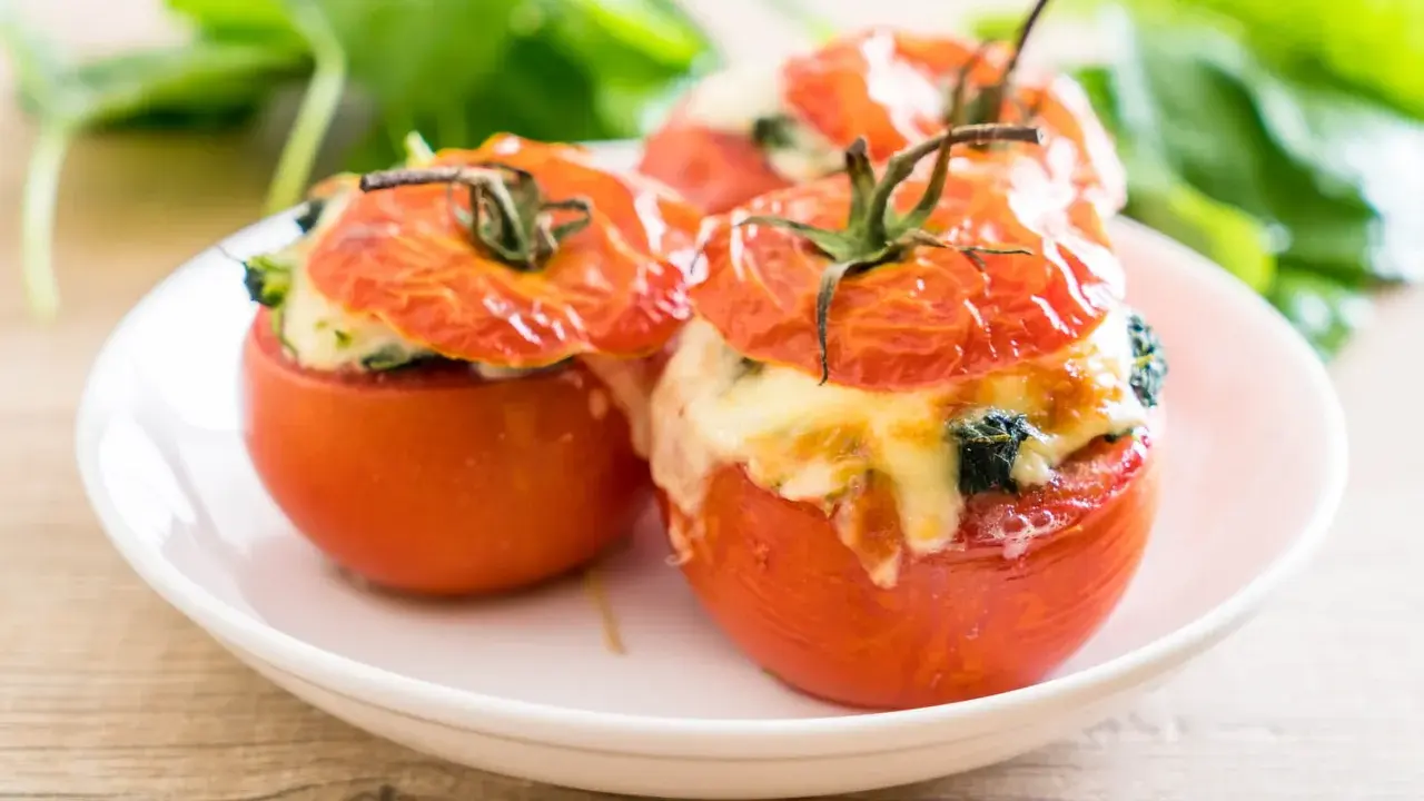 Trois tomates farcies au fromage fondant et aux herbes, servies sur une assiette blanche.