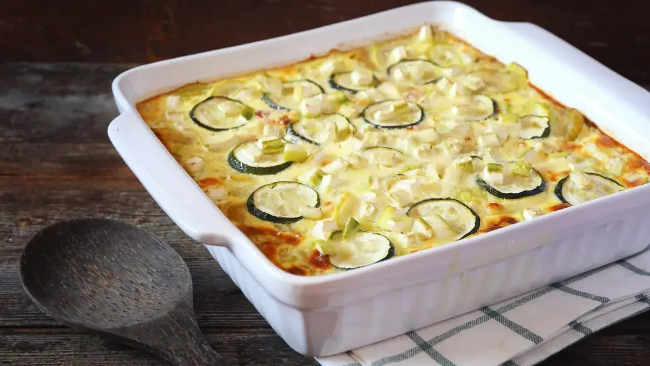 Un gratin de courgettes à l'ancienne, doré et crémeux, garni de rondelles de courgettes et de poireaux, prêt à être dégusté.