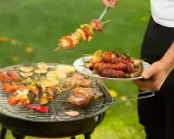 Un homme prépare un barbecue avec des brochettes et des saucisses. Qui a inventé le barbecue ? Mystère !