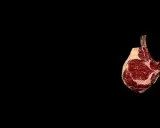 Un morceau de t bone boeuf, avec son os apparent, est présenté sur fond noir. Son emplacement est sur la droite de l'image.