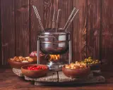 Un appareil à fondue bourguignonne chauffe, entouré de bols de croûtons, d'olives, de tomates séchées et de dés de viande. Idéal pour savoir que faire avec de la viande à fondue bourguignonne.