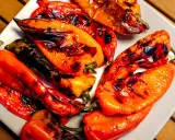 Poivrons rouges et orangés grillés au barbecue, légèrement noircis par la cuisson, sur une assiette blanche.