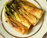 Pak choi braisé, tendre et savoureux, nappé d'une sauce dorée, servi sur une assiette élégante.