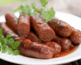 Assiette de merguez au four, dorées et juteuses, garnies de persil frais. Un délice prêt à être dégusté.