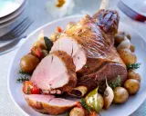 Un gigot d'agneau rôti, tranché, servi avec des pommes de terre nouvelles, tomates et ail. Parfait pour savoir que faire avec des morceaux de gigot d'agneau.