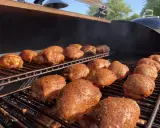 De nombreuses cuisses de poulet désossées, assaisonnées et grillées, fument sur un barbecue par une journée ensoleillée.