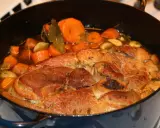 Rouelle de porc mijotant dans une cocotte avec des carottes, de l'ail et des herbes.