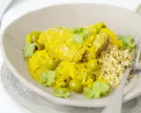 Un plat de tajine poulet citron, garni d'olives vertes et de coriandre fraîche, servi avec du couscous.