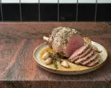 Un délicieux roti d'agneau au four, tranché et servi avec de l'ail rôti et des herbes sur une assiette.