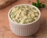Sauce pour viande froide crémeuse avec des morceaux d'œufs durs et des herbes fraîches, servie dans un ramequin blanc sur une table en bois.
