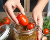 Mains ajoutant une tomate dans un bocal pour une recette de tomate farcie le parfait.