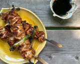 Brochettes yakitori savoureuses, laquées et grillées, servies sur une assiette jaune avec une sauce foncée à côté.