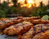 Assiette de poulet boucané grillé, garnie d'herbes et d'une tranche de citron vert, au coucher du soleil.
