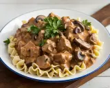 Un plat de boeuf Stroganoff crémeux avec des champignons et des pâtes ondulées, garni de persil frais. Un délice réconfortant.