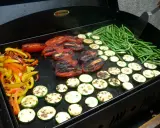 Légumes variés (poivrons, courgettes, tomates, haricots verts) en cours de cuisson sur une plancha. Le temps de cuisson des légumes à la plancha est idéal pour un repas sain et savoureux.