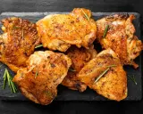 Pile de haut de cuisse de poulet grillé, assaisonné d'herbes et de poivre, sur une ardoise noire.