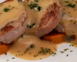 Tranches de gigot d'agneau nappées d'une sauce onctueuse au fond de veau, parsemées de persil et de câpres, sur un lit de carottes.
