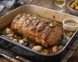 Un rôti de porc au four, doré et juteux, baignant dans son jus avec ail et herbes. Un délice prêt à être dégusté.