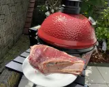 Une belle côte de bœuf crue attend sur une assiette blanche, prête à être grillée sur le barbecue rouge vif.