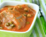 Tranches de langue de bœuf mijotées dans une sauce tomate onctueuse avec des petits pois. Un plat réconfortant servi dans un bol vert vif.