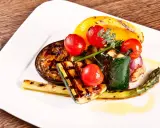 Légumes grillés : courgette, tomate, poivron jaune, aubergine, asperge et oignon rouge, arrosés d'une huile dorée.