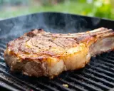Un gros morceau de bœuf sur un gril, fumant doucement. La cuisson lente au barbecue révèle une croûte dorée et une chair juteuse.