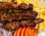 Brochettes de viande grillée, parfaites pour une cuisson indirecte au barbecue, accompagnées de frites, pain pita, tomates et oignons.