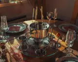Service à fondue prêt pour un repas convivial. Le caquelon en inox est entouré de coupelles et de fourchettes, promettant une fondue sans huile savoureuse.