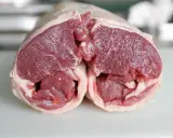 Un plat avec agneau cru, coupé en deux, révélant la chair rouge vif et le gras blanc. Prêt pour une cuisson savoureuse.