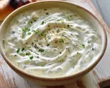 Un bol de sauce blanche crémeuse, garnie d'herbes fraîches et d'épices, prête à accompagner un pain grillé.